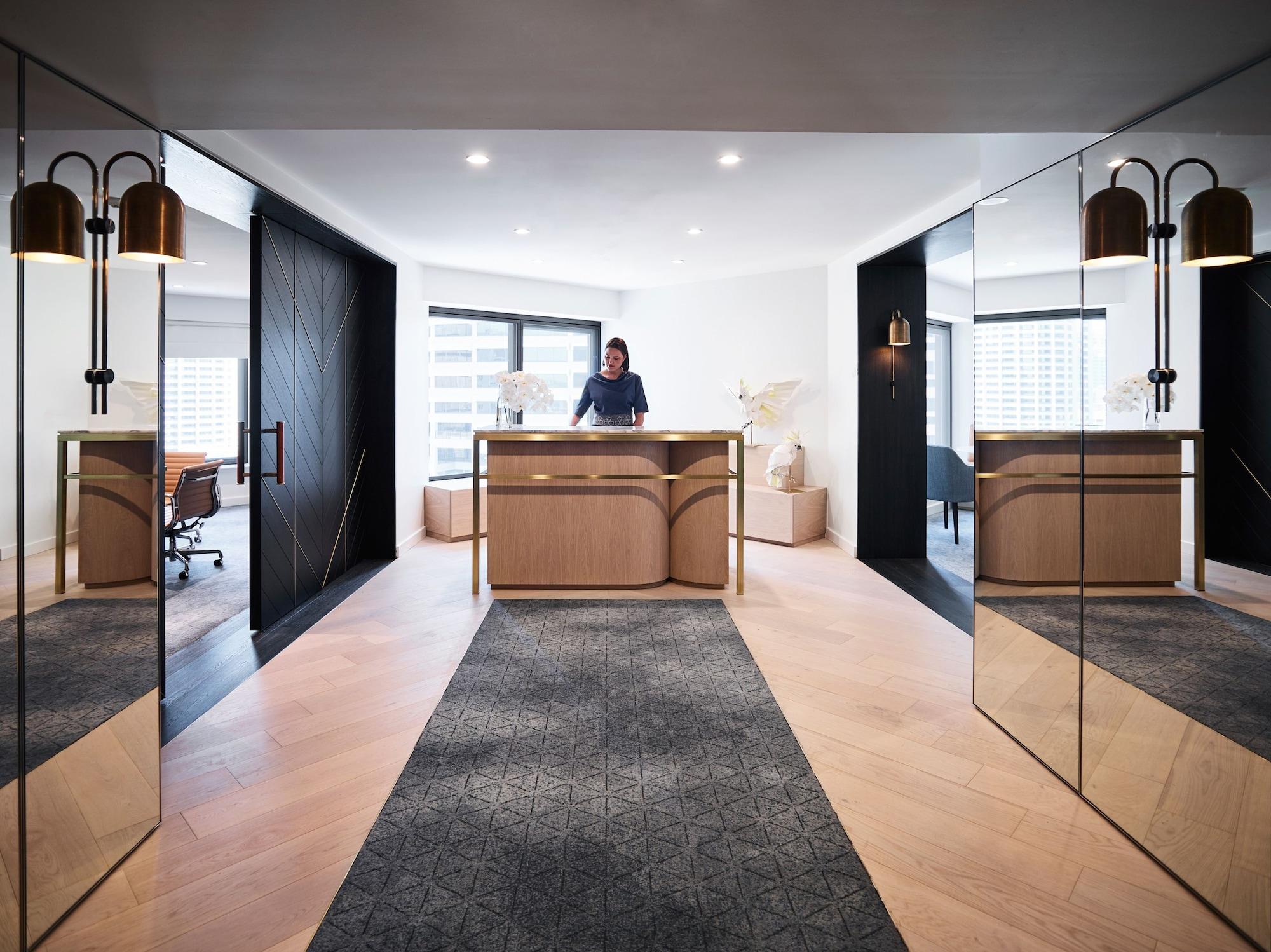 Four Seasons Hotel Sydney Esterno foto The photo shows a modern reception area, characterized by a sleek and stylish design. In the foreground, there is a wooden reception desk with a person standing behind it, likely greeting guests. The desk has a minimalist aesthetic, complemented by d