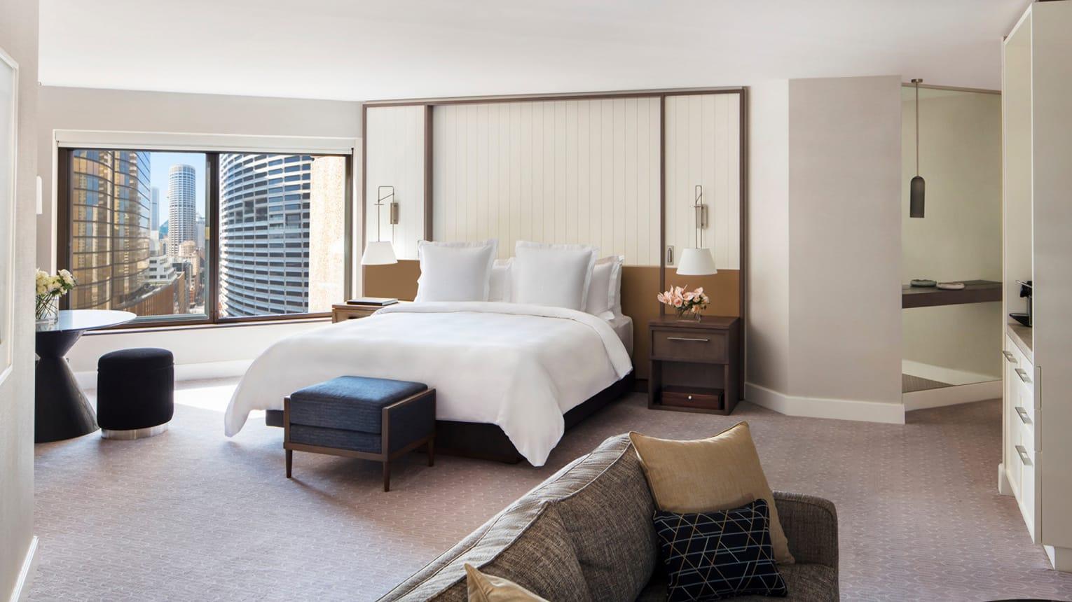Four Seasons Hotel Sydney Esterno foto The photo shows a modern hotel room featuring a spacious layout. In the center is a large bed with plush white linens and two fluffy pillows. On either side of the bed, there are sleek bedside tables with lamps. At the foot of the bed, there's a smal