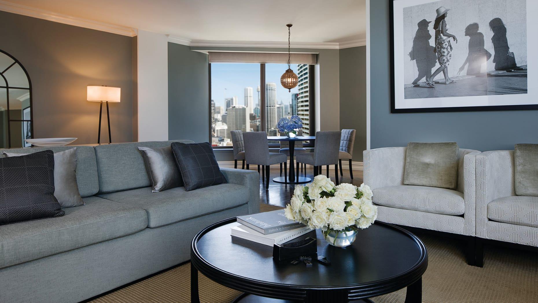 Four Seasons Hotel Sydney Esterno foto The photo shows a modern living room with a stylish and contemporary design. On one side, there is a gray sofa adorned with decorative pillows. A round black coffee table sits in front of the sofa, featuring a vase with white flowers and some books. 