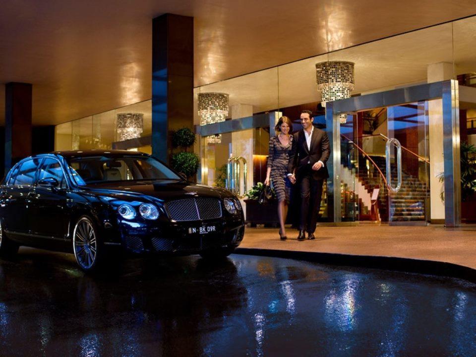 Four Seasons Hotel Sydney Esterno foto The photo depicts a luxurious scene outside a hotel. A sleek black car is parked nearby, and a well-dressed couple is walking hand in hand towards the entrance of the hotel. The surroundings are elegant, with a modern architectural style, and the ent