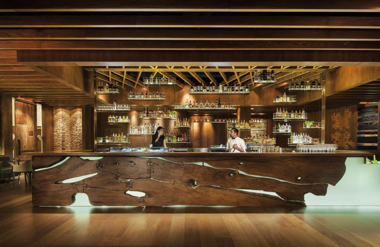 Four Seasons Hotel Sydney Ristorante foto The photo showcases a stylish bar area with a modern design. The bar counter is made of natural wood, featuring a unique, organic shape with visible grain patterns. Behind the bar, shelves hold an array of bottles, suggesting a well-stocked selection