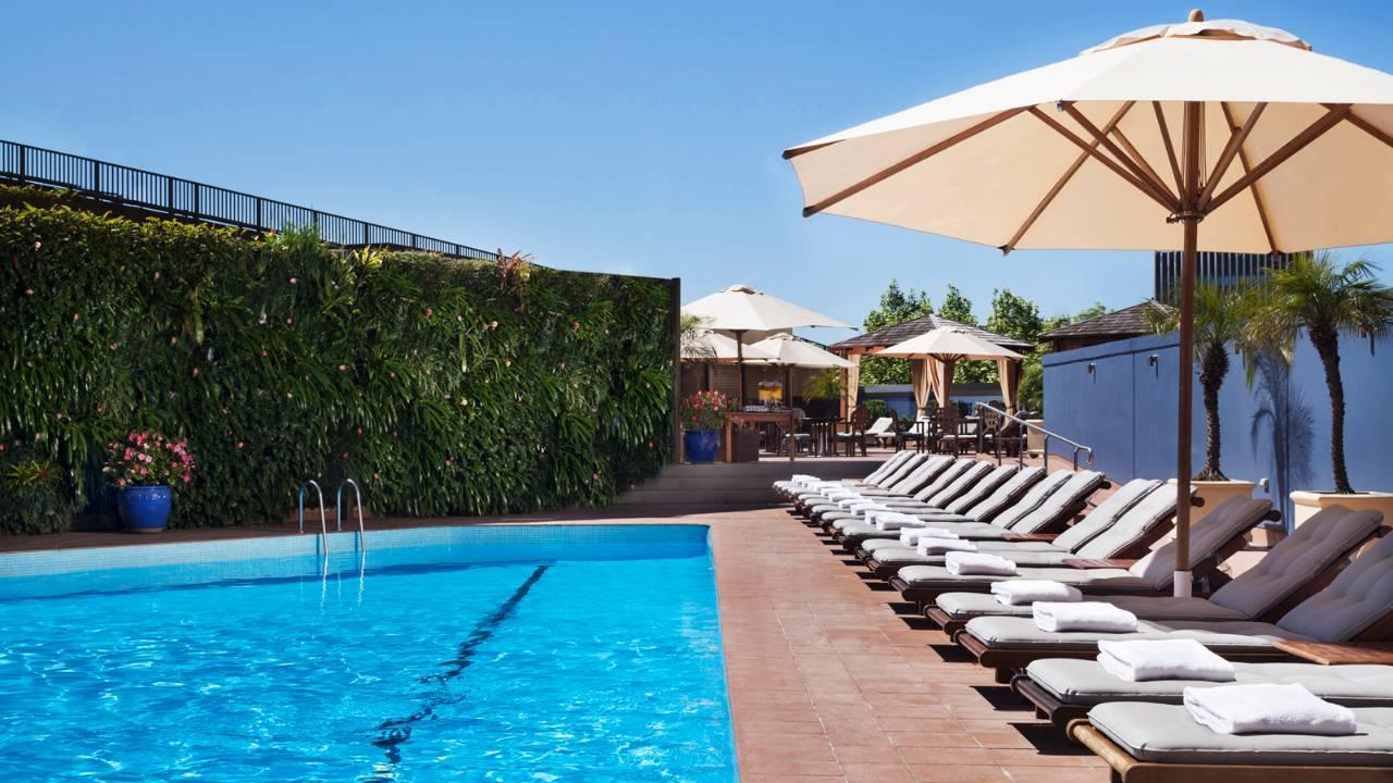 Four Seasons Hotel Sydney Esterno foto The photo shows a beautiful outdoor pool area. The pool has clear blue water and is lined with comfortable lounge chairs. Some of the chairs are shaded by large umbrellas. In the background, there are more umbrellas and seating areas, suggesting a re