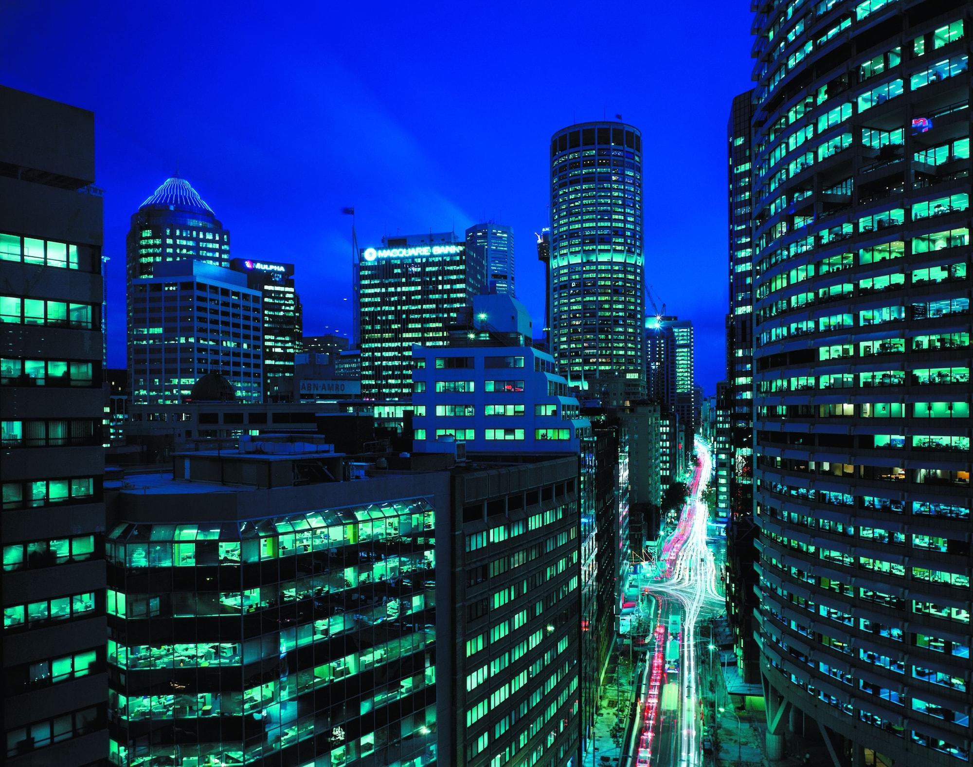 Four Seasons Hotel Sydney Esterno foto The photo showcases a cityscape at night, illuminated by a striking blue and green color palette. Tall skyscrapers dominate the scene, their windows aglow with lights from offices and buildings. The streets below are visible, with lights from vehicle