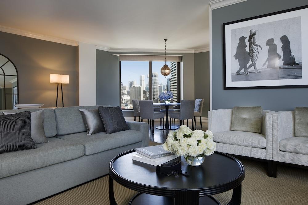 Four Seasons Hotel Sydney Esterno foto The photo showcases a modern living room with a contemporary design. The space features a light gray sofa adorned with darker gray and textured cushions, alongside a matching armchair. A round black coffee table sits in the center, topped with a few 