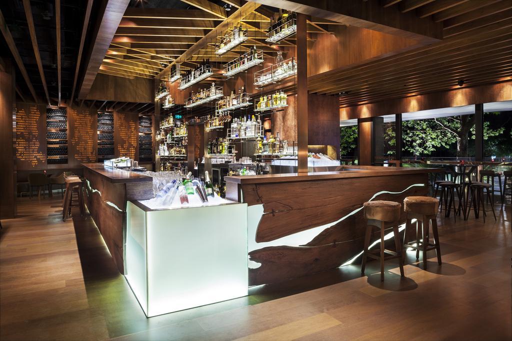 Four Seasons Hotel Sydney Esterno foto The image shows an elegant bar area featuring a sleek design. The bar counter is primarily made of dark wood with a modern illuminated section that has a flowing, wavy pattern. Behind the bar, there are shelves filled with various bottles of spirits 