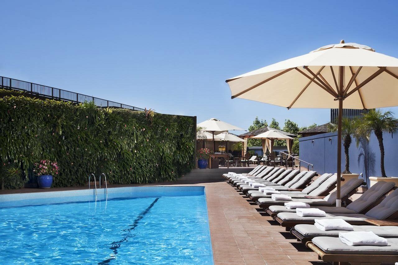 Four Seasons Hotel Sydney Servizi foto The photo shows a swimming pool surrounded by lounge chairs and large umbrellas. The pool itself has clear blue water, and there is a green wall of lush vegetation nearby, providing a natural backdrop. In the background, there are additional shaded s